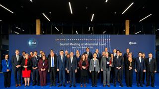 several dozen well-dressed people stand in front of a blue background during a conference